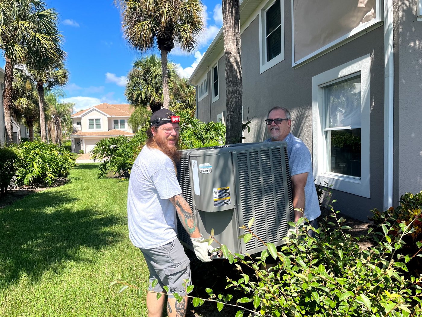 James and Joe Corbett carrying an outdoor air conditioning unit in Fort Myers